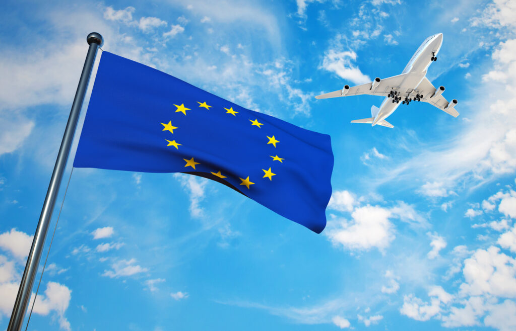 Wehende Europafahne vor blauem Himmel mit fliegendem Flugzeug.