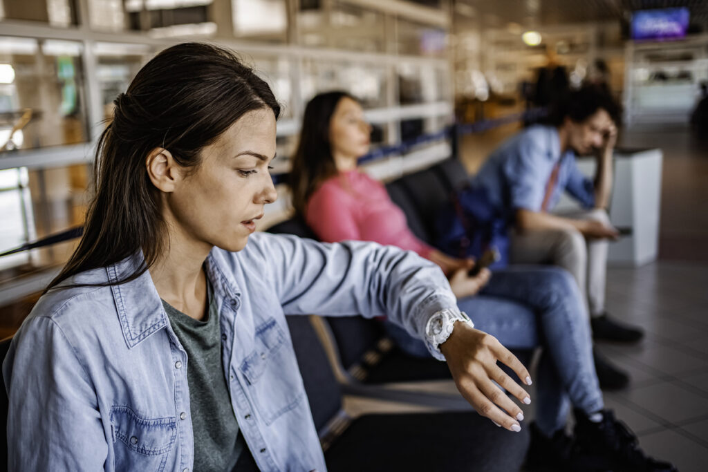 Eine angespannte Frau schaut auf ihre Armbanduhr, während sie auf ihren Abflug am Flughafengate wartet.